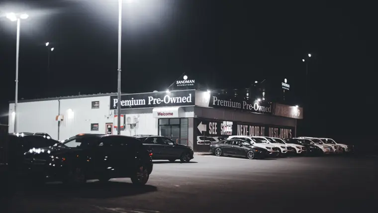 A vehicle lot illuminated by overhead lights after dark