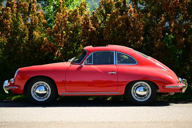 Profile view of a red classic Porsche 356 coupe parked on a road with greenery behind
